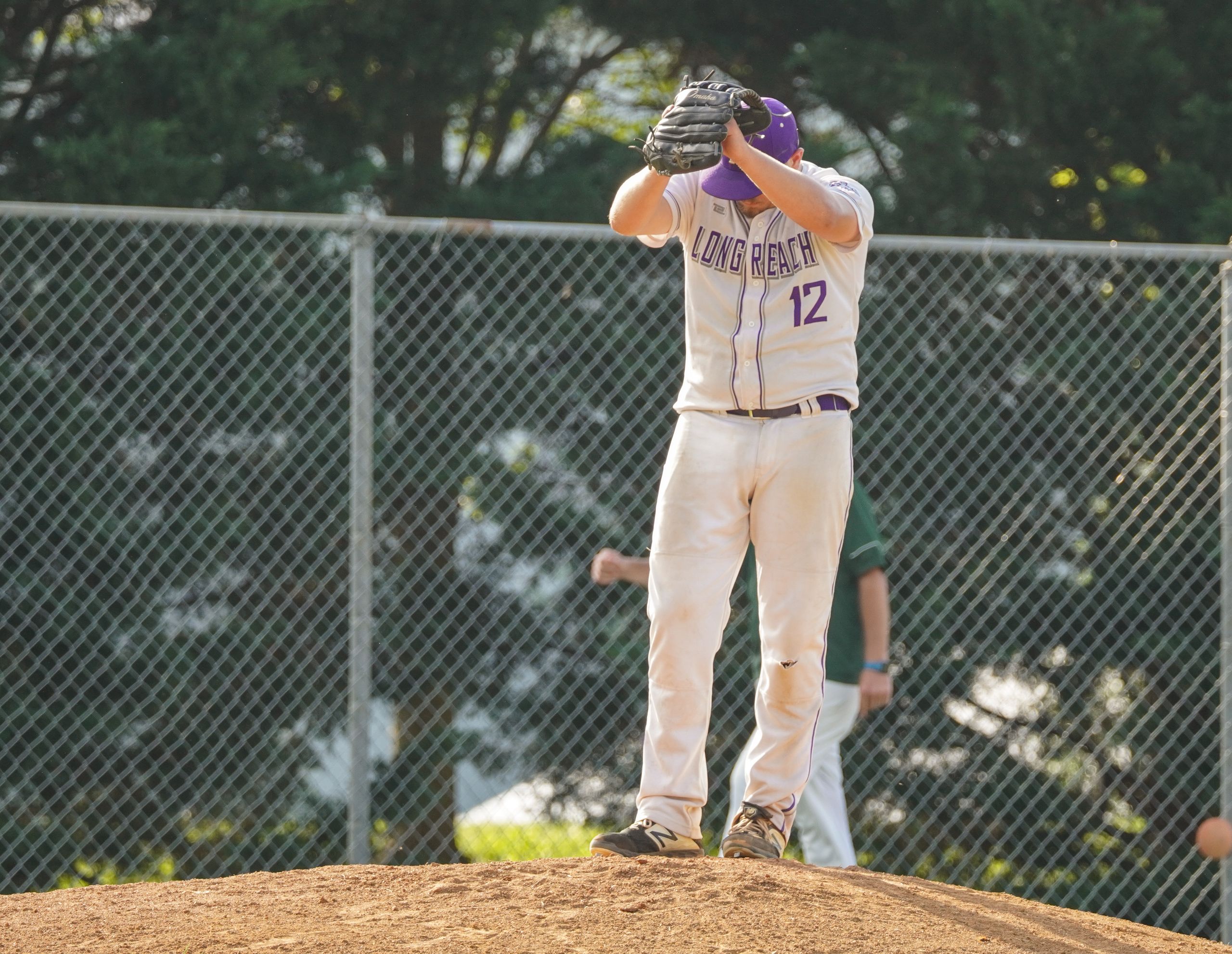 A baseball player in a Long Reach uniform prepares to pitch on a sunny day.