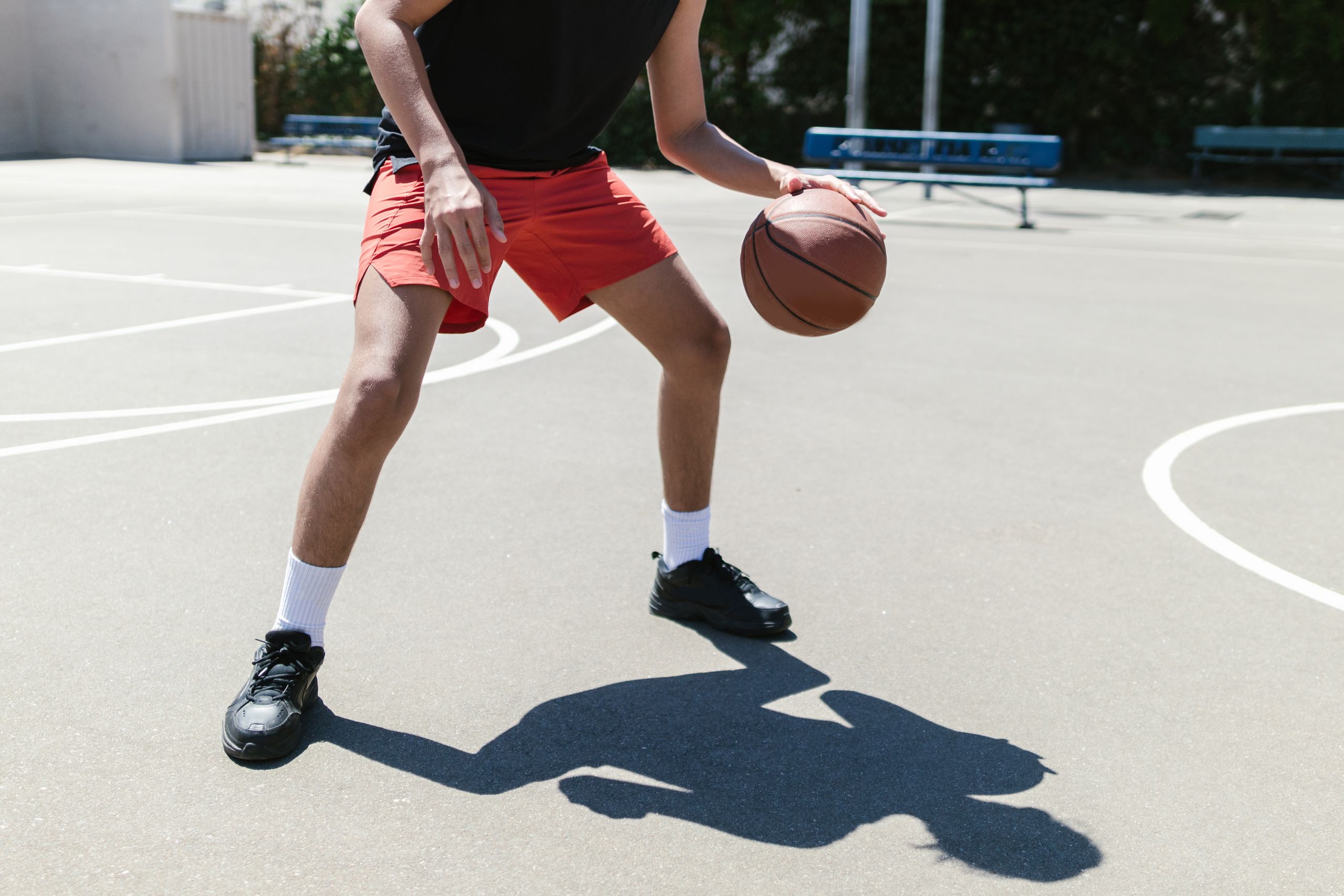 Dynamic shot of an athlete dribbling a basketball on an outdoor court in bright daylight.