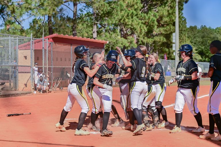 Female softball team celebrating a home run on a sunny day at the field.