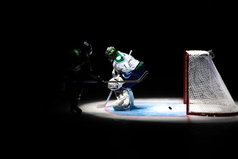Intense ice hockey action with players competing near the goal in dramatic lighting.